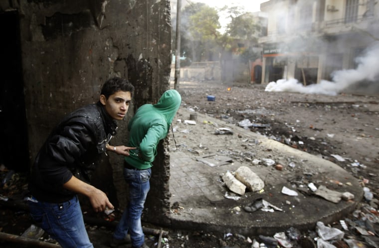 Image: Protesters take shelter behind a wall during clashes with riot police on a side street near Tahrir Square in Cairo