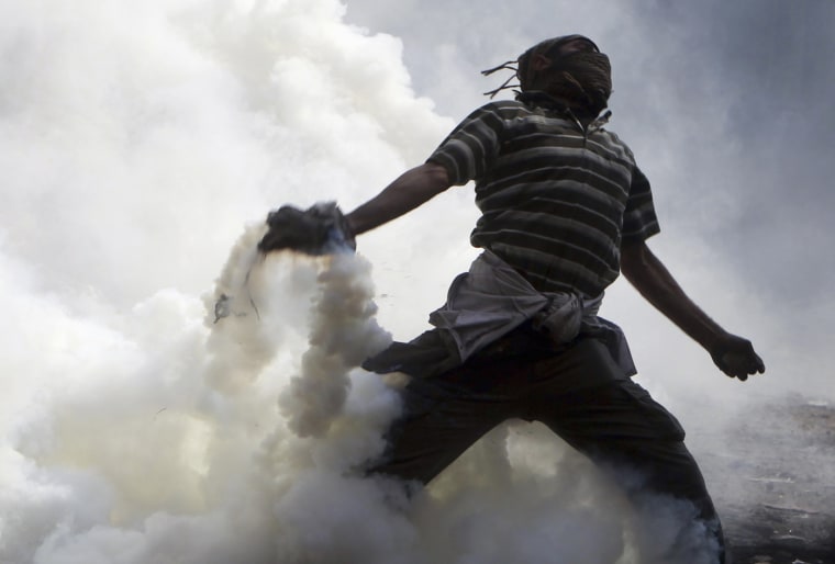 Image: A protester throws a tear gas canister, which was earlier thrown by riot police during clashes along a road which leads to the Interior Ministry, near Tahrir Square in Cairo