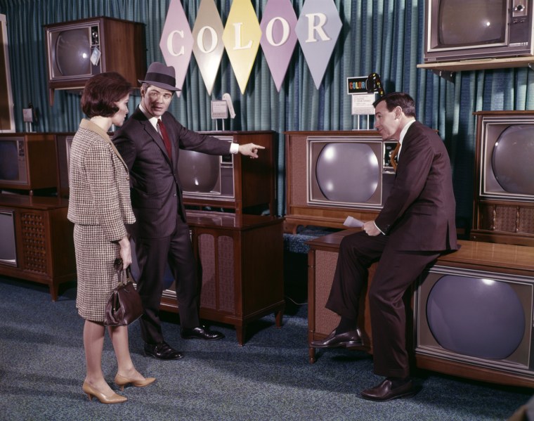 1960s COUPLE MAN WOMAN TALKING TO SALESMAN IN COLOR TELEVISION SET SALES DEPARTMENT. H. ARMSTRONG ROBERTS/CLASSICSTOCK/Everett Collection (ks3560)
