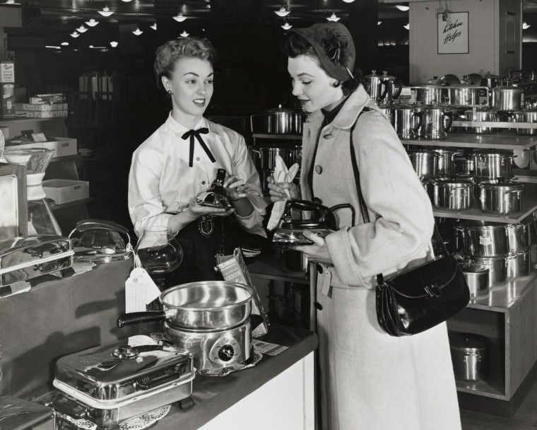 Female sales clerk showing irons to a customer in a store. Photo by: Superstock/Everett Collection(255-384)