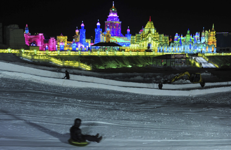 Image: A visitor sleighs down a snow slope near ice sculptures during the lights testing period of the 13th Harbin Ice and Snow World in Harbin