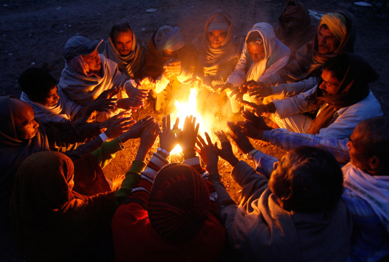 Image: Men warm themselves by a fire at a railway yard on a cold winter morning in Chandigarh