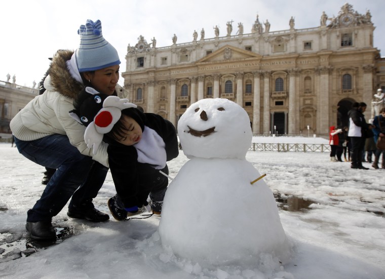 Image: A mother with her son look at a snowman at San Peter square in Vatican