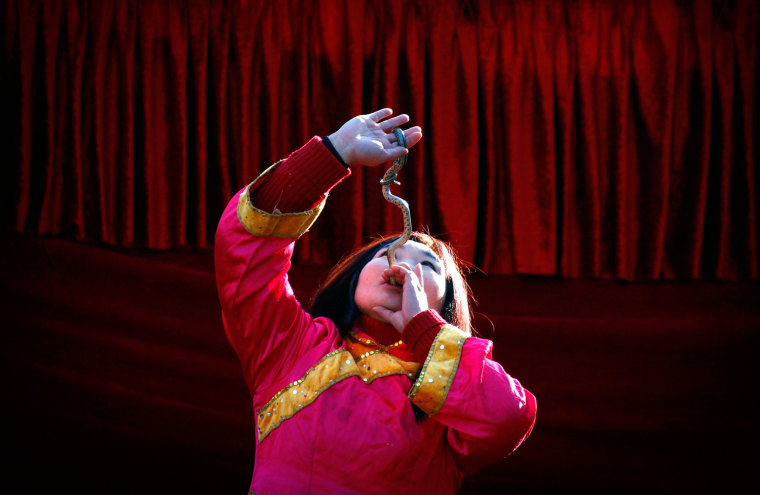 Image: A woman swallows a live snake as she performs on a small stage showcasing acts of magic and feats of unusual physical abilities at the temple fair in Ditan Park