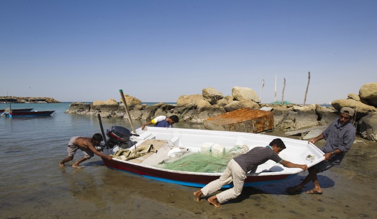 Image: Local Baluch fishermen push a boat to the shore at a fishing port in Tiss village