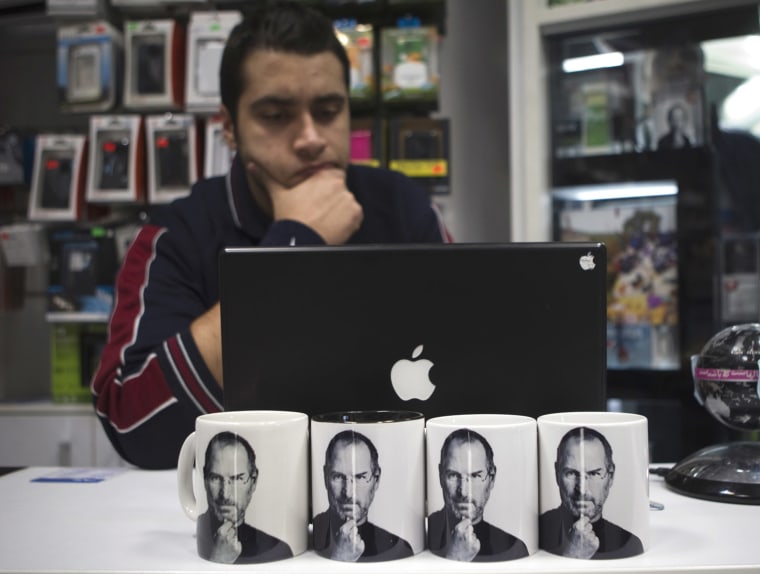 Image: Coffee mugs bearing pictures of the late Apple co-founder Jobs are displayed for sale as a man works on a MacBook at a shop in northern Tehran