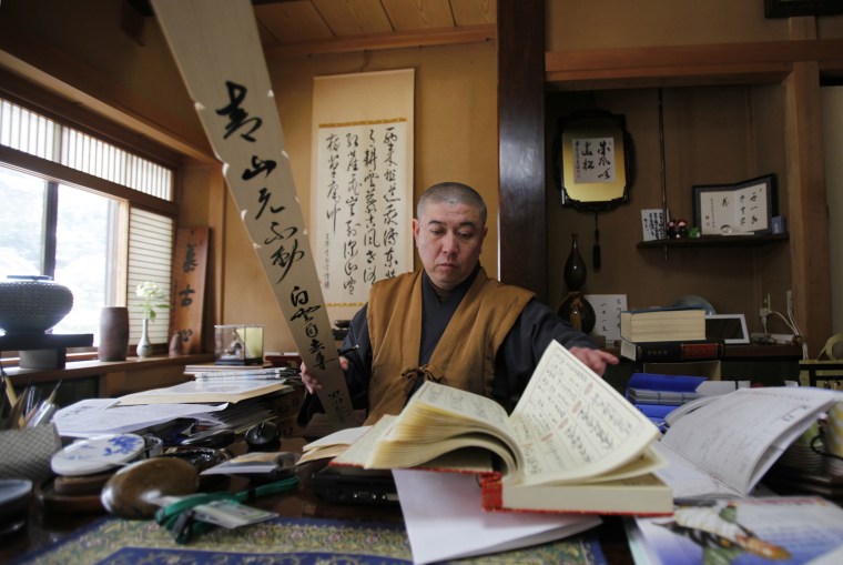 Image: Koyu Abe, a Zen priest, looks through a book as he writes a Buddhist name on a wooden grave tablet at his study room in Joenji temple in Fukushima