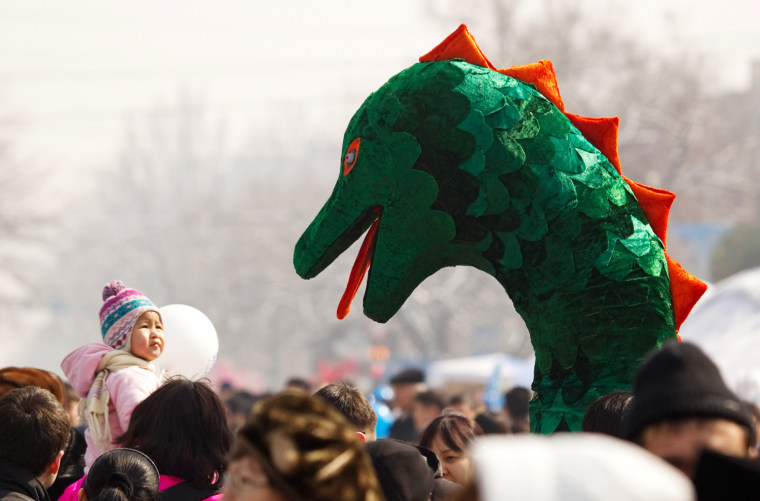 Image: A girl looks at an artist wearing the costume of a dragon during the Nauryz celebration in Almaty