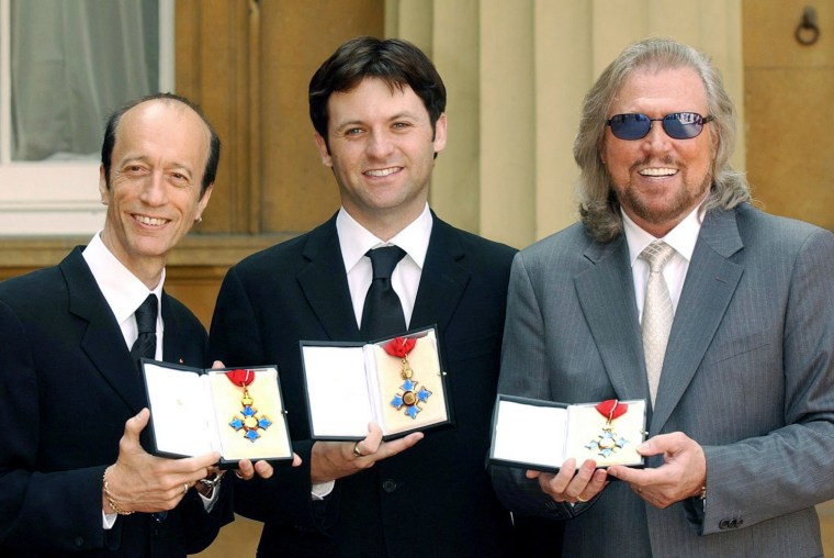 The two surviving members of the Bee Gees, Robin Gibb, left, and Barry Gibb right, hold their CBE's along with Adam Gibb who received the honour on behalf of his father, the late Maurice Gibb, at Buckingham Palace in London, Thursday May 27, 2004. All three brothers were awarded CBE's although Maurice Gibb died last year before he could receive the honour. (AP Photo/John Stillwell, pool)