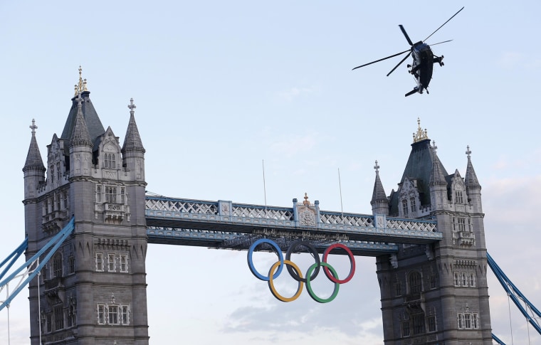 Image: A Royal Navy helicopter carrying the London 2012 Olympic torch flies over Tower Bridge in London