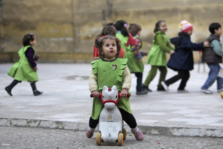 Image: A girl looks up to sky after hearing sound of shelling as she sits on toy pony in playground of Al-Tawheed school in Aleppo
