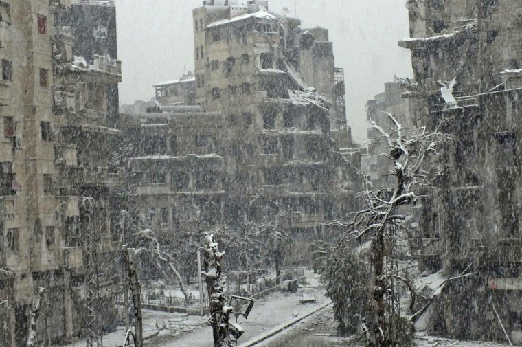 Image: Snow falls over damaged buildings at Jouret al Shayah area in Homs
