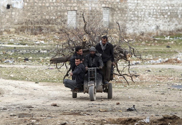 Image: People ride on a motorbike loaded with pieces of wood for heating in Karm al-Tarab neighborhood in Aleppo