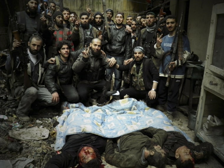 Image: Free Syrian Army fighters carry their weapons as they pose next to bodies of forces loyal to Syria's President Bashar al-Assad in Al-Khalidiya neighbourhood of Homs