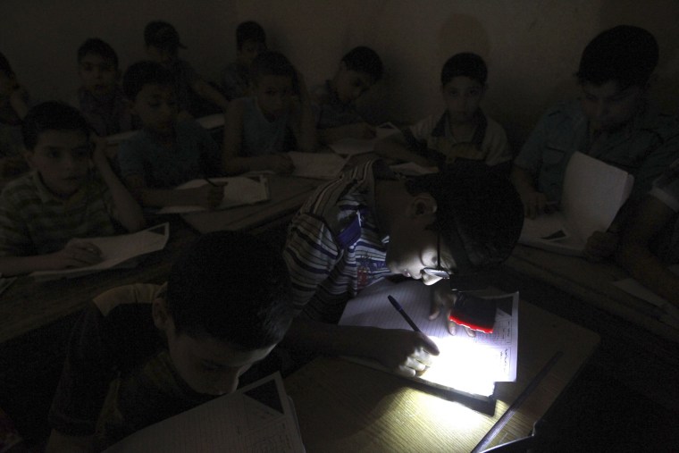 Image: A student wears a headlight, due to electricity shortage, as he takes his year-end examinations at a school in Aleppo's al-Sha'ar district
