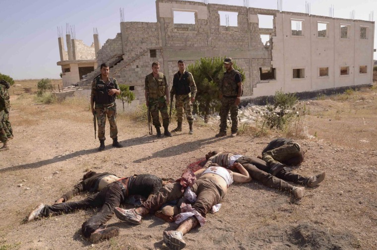 Image: Forces loyal to Syria's President al-Assad stand near dead bodies, which according to forces belong to members of Free Syrian Army, during what they said was military operation against them in al-Mansoura