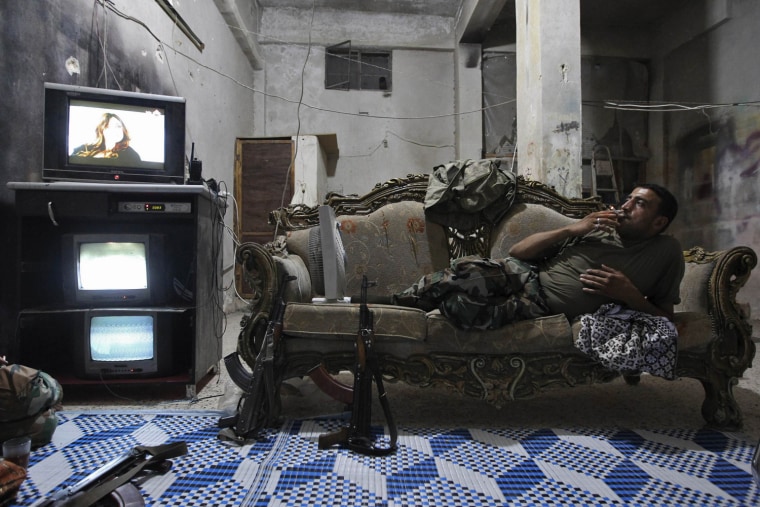 Image: A Free Syrian Army fighter rests on a sofa as he watches televison and surveillance monitors inside a room in Aleppo's Karm al-Jabal district