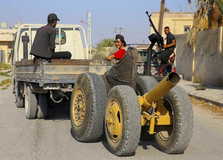 Image: A Free Syrian Army fighter smiles while seated on a truck pulling an improvised mortar launcher as a fellow fighter stands on a back of another truck mounted with an anti-aircraft gun in al-Ghouta region in the eastern rural suburbs of Damascu