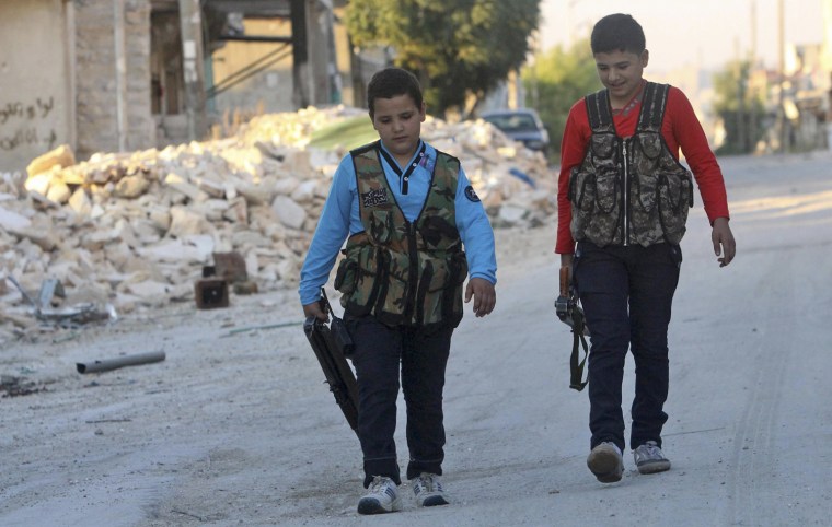 Image: Abboud and his brother Deeb walk with their weapons in Aleppo