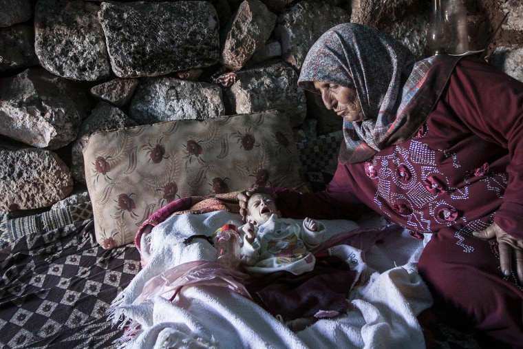 Image: A displaced Syrian woman comforts her one-month old grandchild Fatima inside a stone house near Kafer Rouma, in ancient ruins used as temporary shelter by families who have fled from fighting