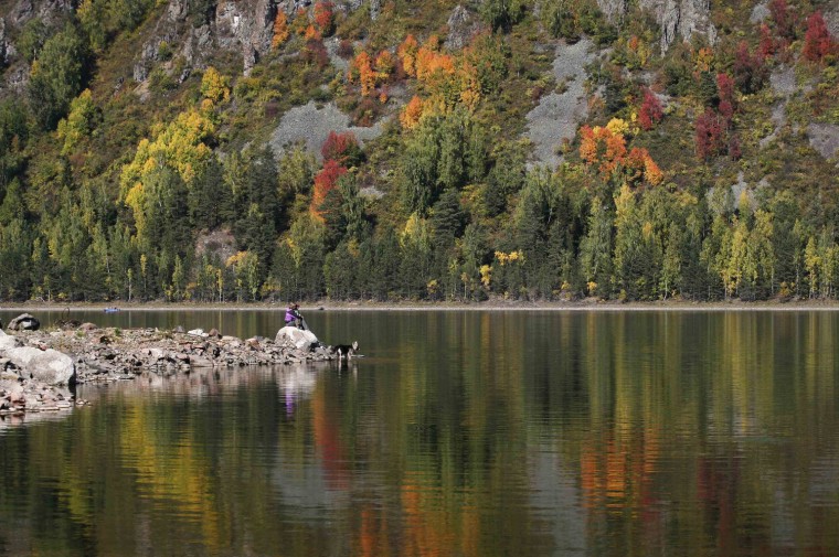 Image: Local residents sit on a bank of the Yenisei River surounded by reflection of the Siberian taiga in autumn foliage south of the city of Krasnoyarsk
