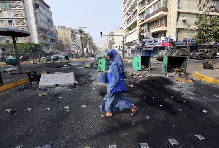 Image: A woman crosses a street, blocked with garbage bins and barricades placed by protesters against the killing of senior intelligence official Wissam al-Hassan in an explosion, in Beirut
