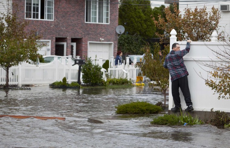 Image: A man attempts to walk across a fence surrounded by flood waters in Staten Island