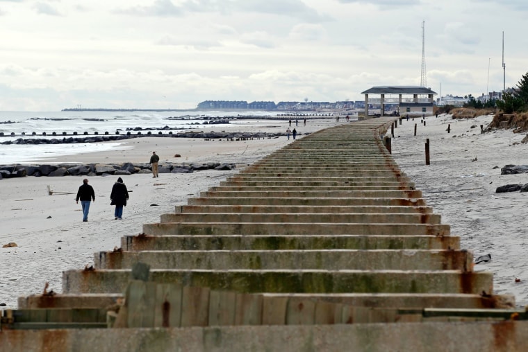 Image: People walk on the beach past the remnants of the Spring Lake boardwalk which was damaged by Hurricane Sandy in Spring Lake