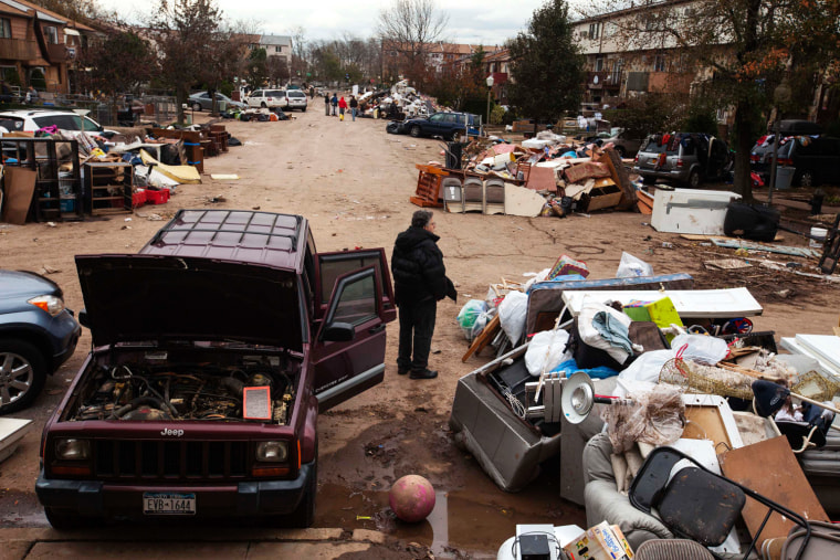 Image: A man stands next to a damaged vehicle as he surveys flood damaged personal property thrown into the streets in the New Dorp Beach neighborhood