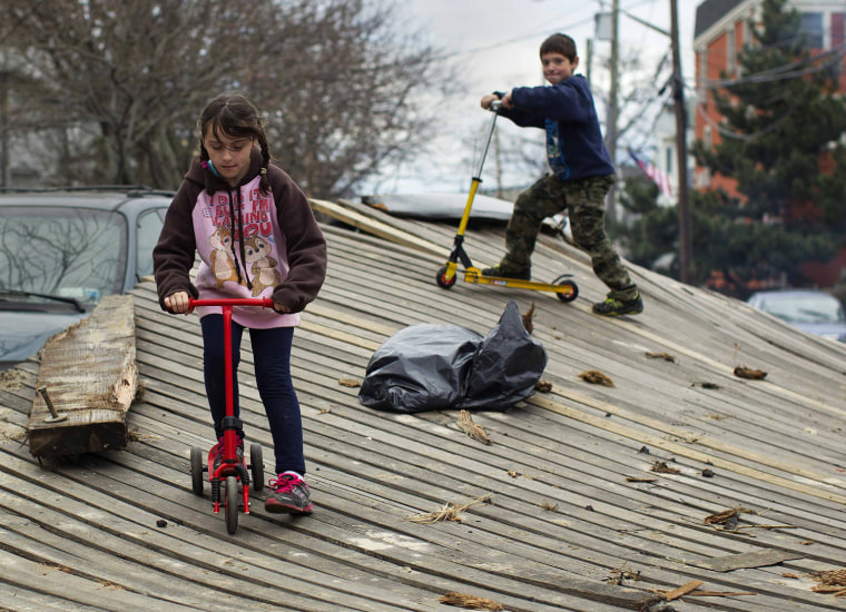 Image: Children ride their scooters on a piece of boardwalk that was washed on a street in New York