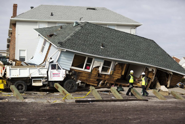 Image: Workers pause to look at a home that has been pushed on top of a work truck by the storm surge of Hurricane Sandy in the Brooklyn borough region of Belle Harbor in New York