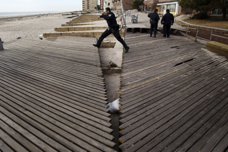 Image: An NYPD officer jumps over a chasm in the boardwalk caused by the storm surge of Hurricane Sandy in the Brooklyn borough region of Belle Harbor in New York