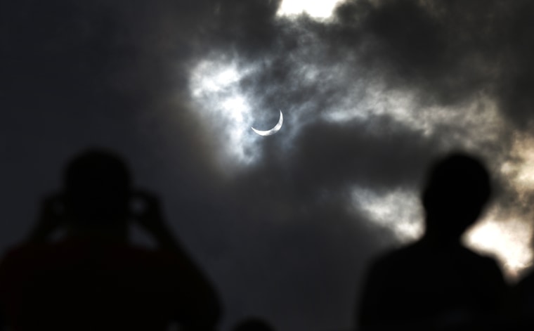 Image: Tourists watch as the moon blocks the sun as it approaches a full solar eclipse in the northern Australian city of Cairns