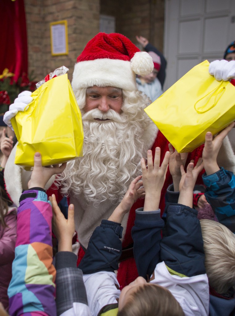 Image: Children reach for presents distributed by a man dressed as Santa Claus outside the post office in the village of Himmelpfort