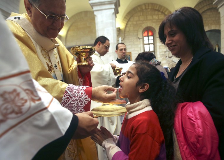 Image: A Palestinian girl receives communion from the Latin Patriarch of Jerusalem Twal at the Church of St. Catherine in Bethlehem on Christmas day