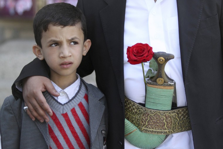 Image: A boy looks on as he stands with his father with a rose placed on his belt while they shop for gifts on Valentine's Day in Sanaa