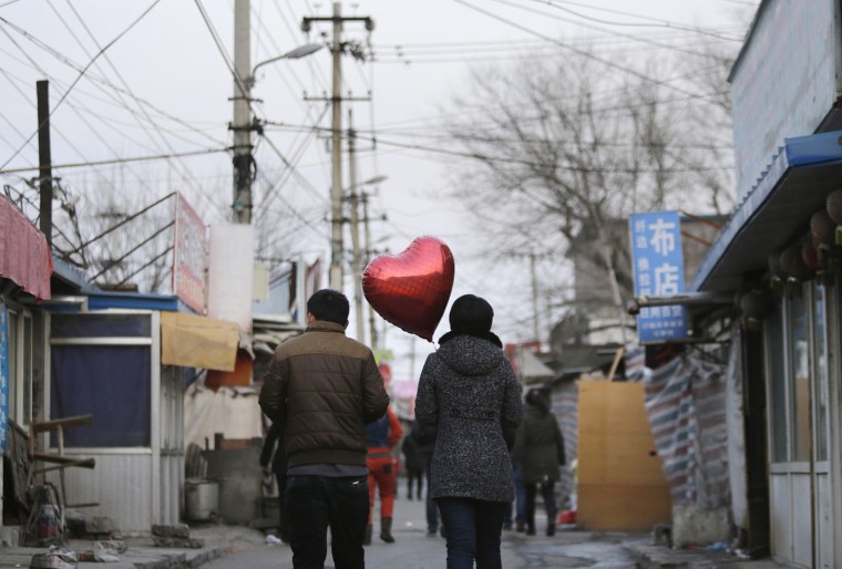 Image: A woman holding a heart-shaped balloon walks with her partner at a residential area for migrant workers on Valentine's Day in Beijing