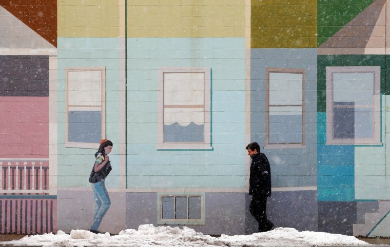 Image: A pedestrian walks past a mural at the beginning of a winter storm in Somerville