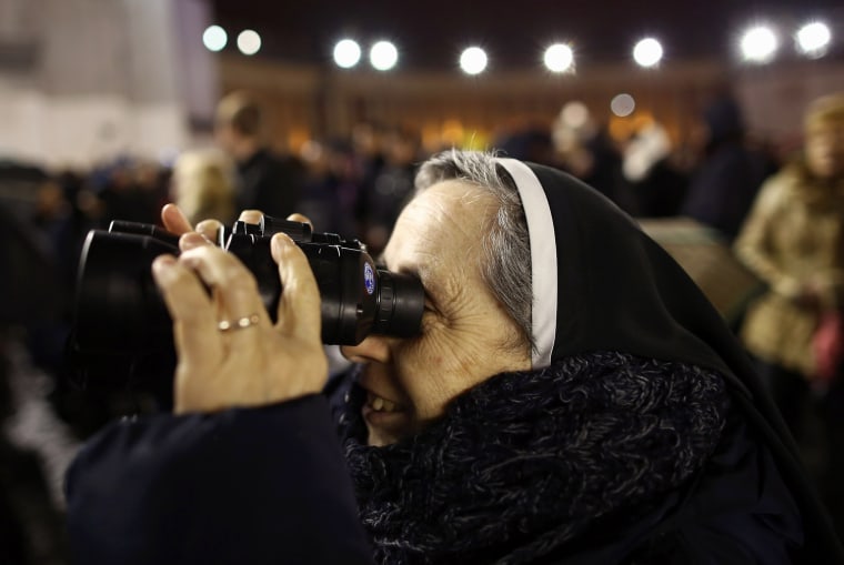 Image: A nun looks through binoculars as people wait for an indication as to whether the College of Cardinals have elected a new Pope.