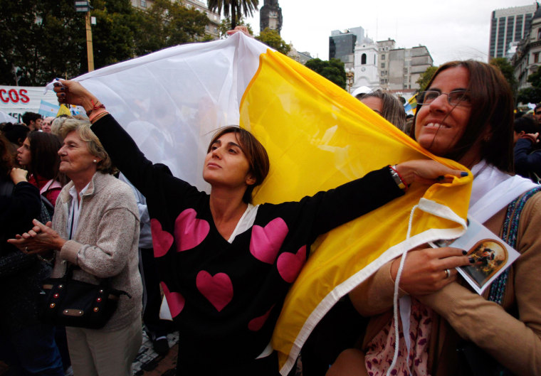 Image: A woman holds a Vatican flag as she and other faithful watch a televised broadcast of the inaugural mass of Pope Francis near the Metropolitan Cathedral in Buenos Aires