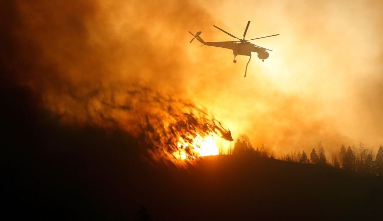 Image: A helicopter air tanker dumps water as the sun sets at the Beaver Creek wildfire outside Hailey