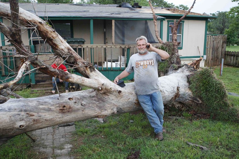 Image: Cook talks on his cell phone as he stands next to a downed tree which missed falling on a home in a mobile home park where several other homes were destroyed by a tornado, west of Shawnee, Oklahoma