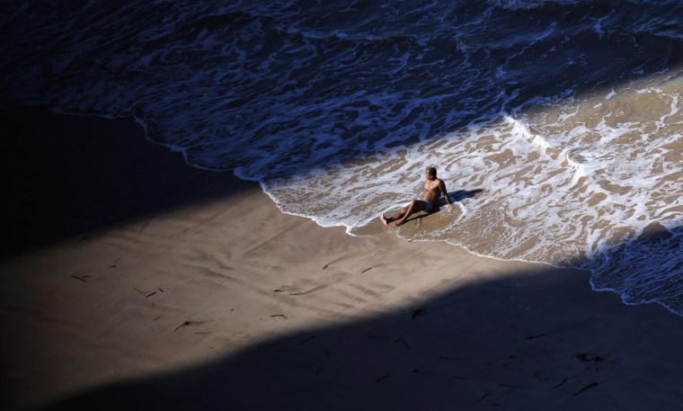 Image: A man sunbathes between the shadows of two buildings on Boa Viagem Beach in Recife