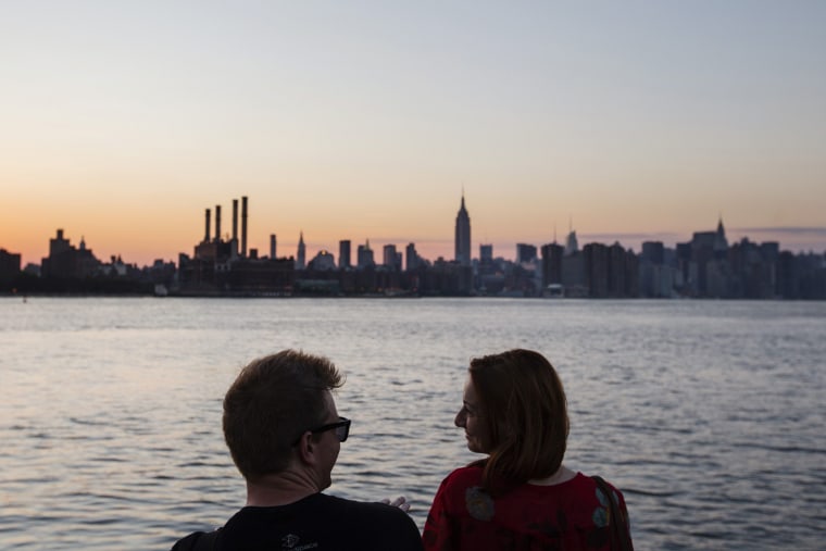 Image: A couple laughs as they watch the sun set behind the skyline of New York
