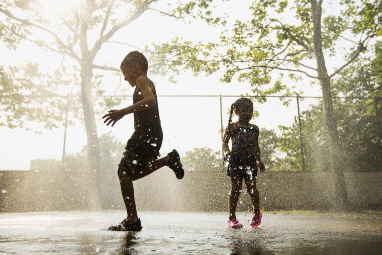 Image: Children run through a sprinkler system installed inside a playground to cool off during a hot summer day in New York