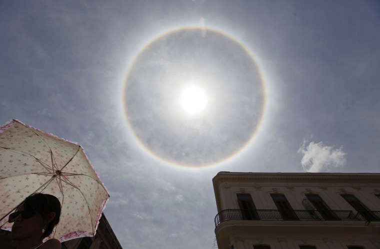 Image: A woman walks on a street with her umbrella as an atmospheric phenomenon known as a \"sun dog\" is seen in the sky over Havana