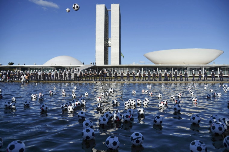 Image: Soccer balls marked with red crosses float after being kicked as a protest by members of NGO Rio de Paz into the fountain in front of National Congress in Brasilia