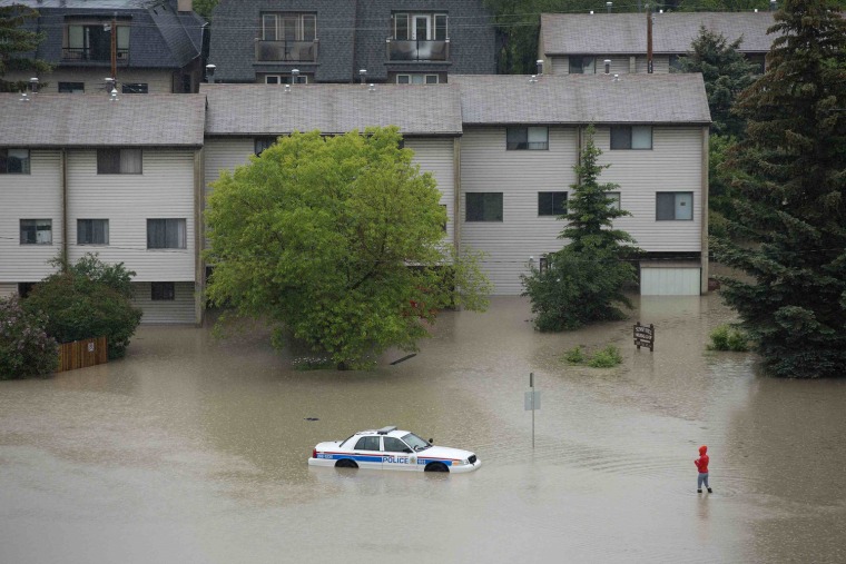 Image: A woman looks at an abandoned and partially submerged police car after flooding from Bow River hit the neighbourhood of Sunnyside in Calgary