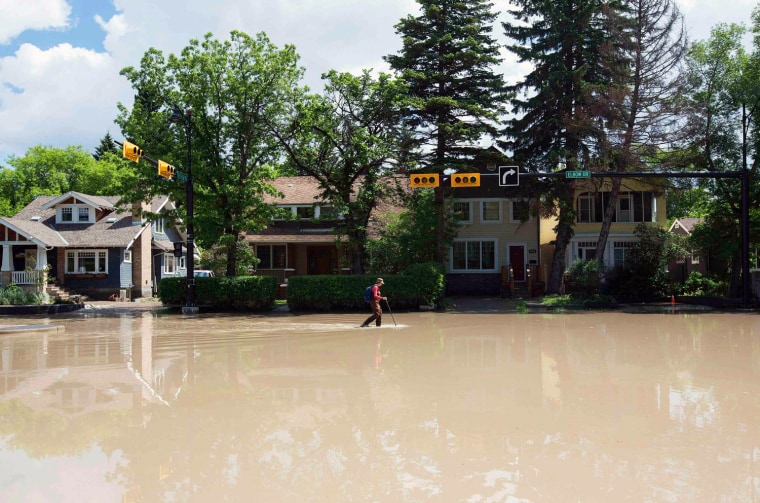Image: A woman walks down a flooded street in the Elbow Park area of Calgary