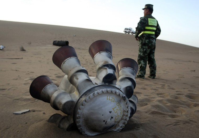 Image: Policeman stands guard next to a component of the Shenzhou-10 manned spacecraft which was found in Badain Jaran Desert after the launch, in Alxa League